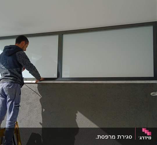 אדם עובד על התקנת חלון אלומיניום במרפסת